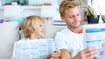 Cute happy kid looking at dad while dad reads news paper 