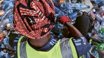 A person sitting in a pile of plastic bottles and sorting them. A person sitting in a pile of plastic bottles and sorting them.