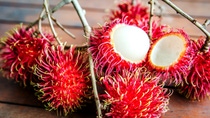 Half-separated rambutan from a skin on a wooden table among whole fruits.