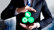 A man in a suit holding two hands in front of him and three icons photoshopped to show in between his hands to symbolize sustainability. 