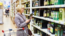 Woman reading the label on a bottle of olive oil in the store Woman reading the label on a bottle of olive oil in the store