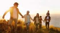 Happy family holding hands walking up hill in a line with sun shining 