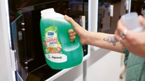 Person fills detergent into a container at a vending machine. Person fills detergent into a container at a vending machine.