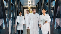 Three men and a woman in white working coats walking.
