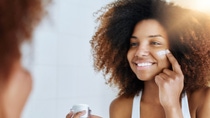 A young woman applying cream on her face.