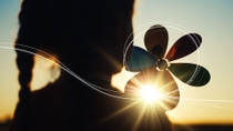 A silhouette image of a child with a rainbow coloured pinwheel, looking at the sunset setting on the horizon, with sketch lines showing the path of the wind over her pinwheel.