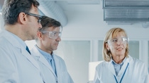two men and two women scientists wearing safety goggles having a discussing  