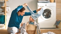 Beautiful young woman and child girl little helper are having fun and smiling while doing laundry at home.