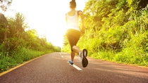 A woman in sporty clothes running down an empty road towards a setting sun.