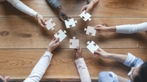 Startup and teamwork concept, top view of creative multiracial team sitting at table and putting together puzzle pieces Startup and teamwork concept, top view of creative multiracial team sitting at table and putting together puzzle pieces