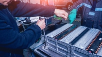 Two people in blue uniform work on batteries.