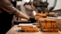 Wooden boards lying on a table. In the background a man is working with the wooden boards.