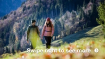 A man and woman are walking across a mountain meadow on a sunny day. They are wearing warm outdoor clothing. A man and woman are walking across a mountain meadow on a sunny day. They are wearing warm outdoor clothing.