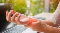 Closeup woman holding her painful hand from using computer. Office syndrome hand pain by occupational disease.