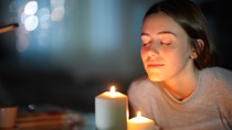 Woman smelling a lighted candle in the night Woman smelling a lighted candle in the night