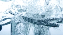 A close-up of forks and glasses submerged in water with bubbles surrounding them.