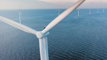 Close-up of the rotor of a wind turbine taken from bird perspective, with more wind turbines in the backdrop, standing in a row in a sea with waves. Close-up of the rotor of a wind turbine taken from bird perspective, with more wind turbines in the backdrop, standing in a row in a sea with waves.