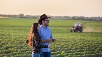 A man and woman standing on a field with a tractor in the background. A man and woman standing on a field with a tractor in the background.