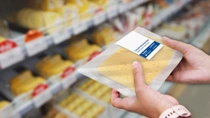 A person is holding a plastic package of sliced cheese in a grocery store. The background features shelves stocked with various types of cheese. A person is holding a plastic package of sliced cheese in a grocery store. The background features shelves stocked with various types of cheese.