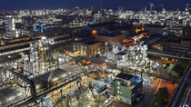 The picture shows an aerial view of the industrial complex divided by dark pipes and lit up by several lights.