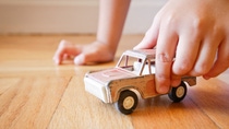 This is a nostalgic image of a young boy playing with an antique toy SUV on a wood floor.