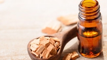 Pieces of sandalwood in a wooden spoon next to a small brown bottle filled with clear liquid