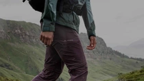 A close-up of a man’s leg in grey Vaude pants, with mountains in the background. A close-up of a man’s leg in grey Vaude pants, with mountains in the background.