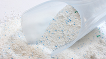 White powder laundry detergent with blue grains pouring out of plastic cup