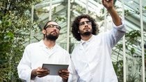 Male scientist pointing while colleague holding digital tablet against greenhouse