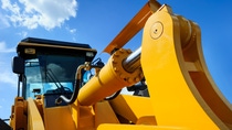 Bulldozer, huge yellow powerful construction machine with big scoop, focused on hydraulic piston arm, heavy industry, blue sky and white clouds on background