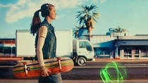 A young woman with headphones walks along a city street holding a skateboard. In the background there are palm trees, buildings, and a truck. A light swirl appears on the road surface. A young woman with headphones walks along a city street holding a skateboard. In the background there are palm trees, buildings, and a truck. A light swirl appears on the road surface.