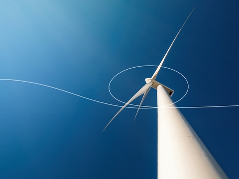 Looking up from the ground at a tall wind turbine against a clear blue sky – scientific equations and sketches highlighting the path of the wind are overlaid on the picture. 