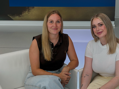Alena Wolf und Tamara Rettig sitzen auf weißen Sesseln in modernem Raum mit großem Wandbild im Hintergrund Alena Wolf und Tamara Rettig sitzen auf weißen Sesseln in modernem Raum mit großem Wandbild im Hintergrund