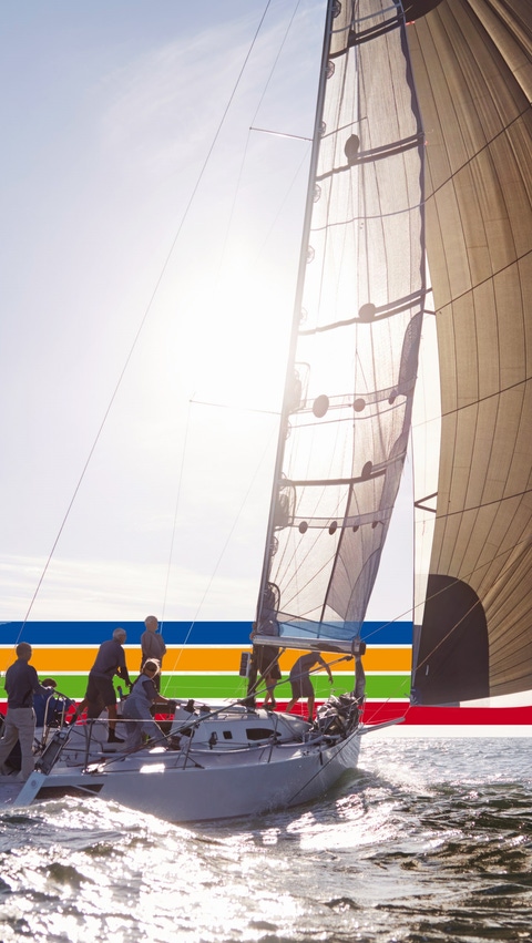 People on a sailing boat in the ocean, under a bright sky, surrounded by a key visual of four lines in blue, orange, green and red (photoshopped) 