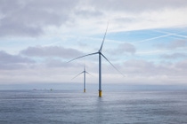 A wind farm under construction. Two wind turbines in a blue ocean. In the backdrop, you can find three more monopile foundations and a ship.