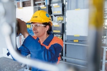 Female engineer in BASF-branded protective clothing and helmet looks into a piece of equipment at BASF’s methane pyrolysis test facility in Ludwigshafen.