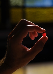 Hand holding a small red mineral fragment. Hand holding a small red mineral fragment.