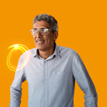A male BASF employee in a grey shirt standing against a orange background, a light swirl hovers around his shoulder. A male BASF employee in a grey shirt standing against a orange background, a light swirl hovers around his shoulder.